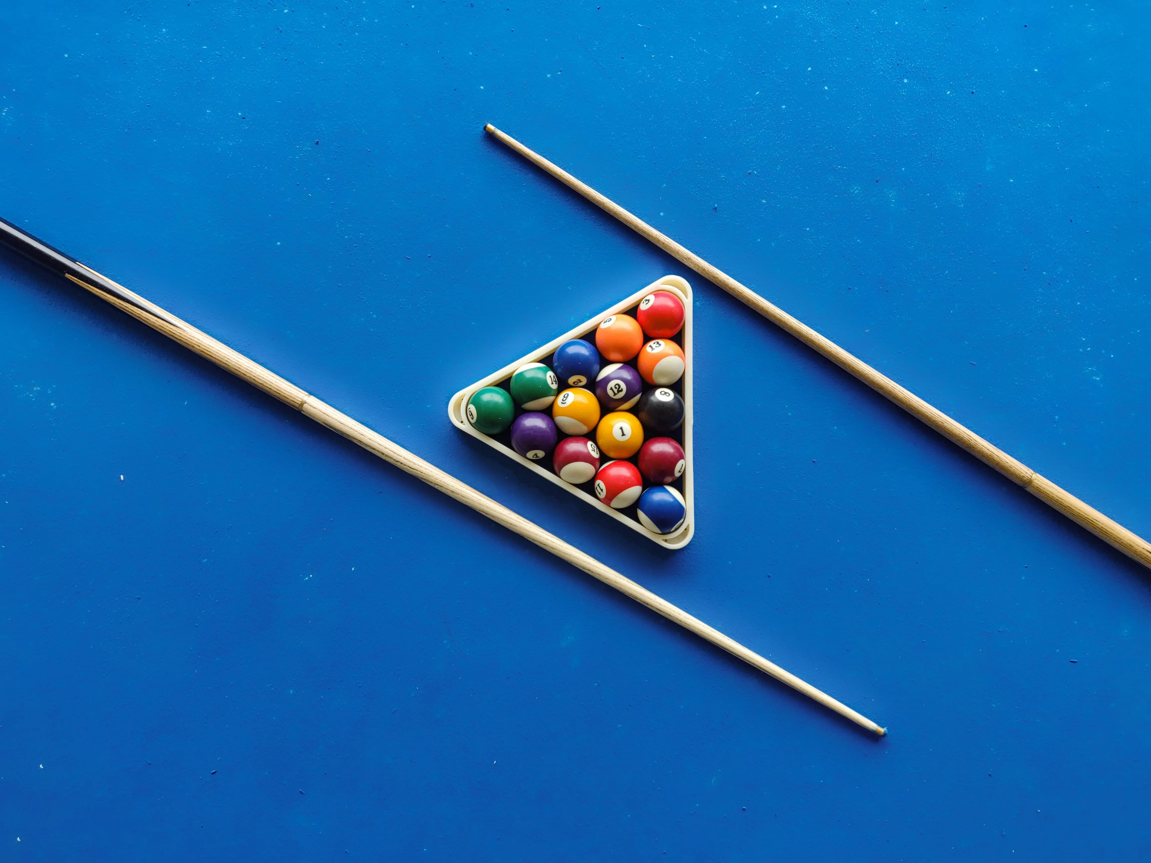 Cue sticks crossed on a billiards table with cue ball and racked billiard balls